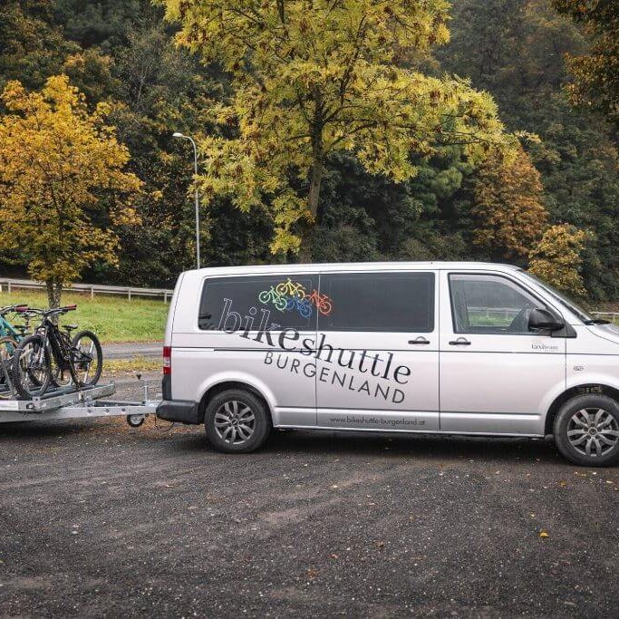 Bike Shuttle Burgenland Van mit Fahrradanhänger, geparkt auf einem Rastplatz im Grünen – symbolisiert den Fahrradtransport-Service vom Taxi Team Loibl in Kooperation mit den Burgenland Trails.