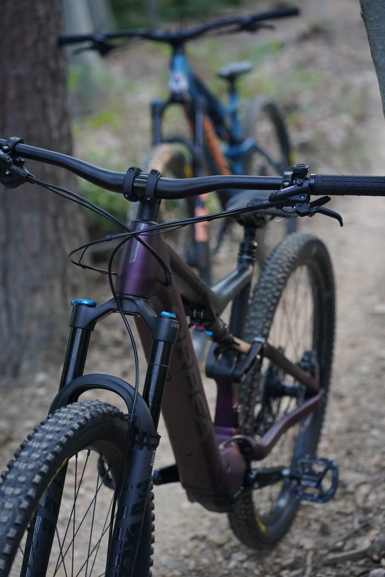 Zwei moderne Fully-Mountainbikes stehen auf einem schmalen Waldweg, im Vordergrund ein matt-lilanes Modell mit breiten Reifen – bereit für den Einsatz auf den Trails rund um den Geschriebenstein.